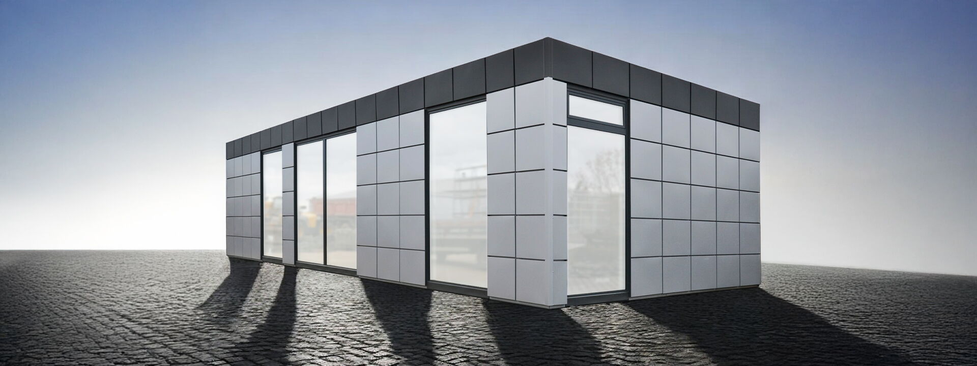 Moderne kantoorcontainer met grijze rastergevel en grote vloerdiepe ramen op een bestraat oppervlak      
