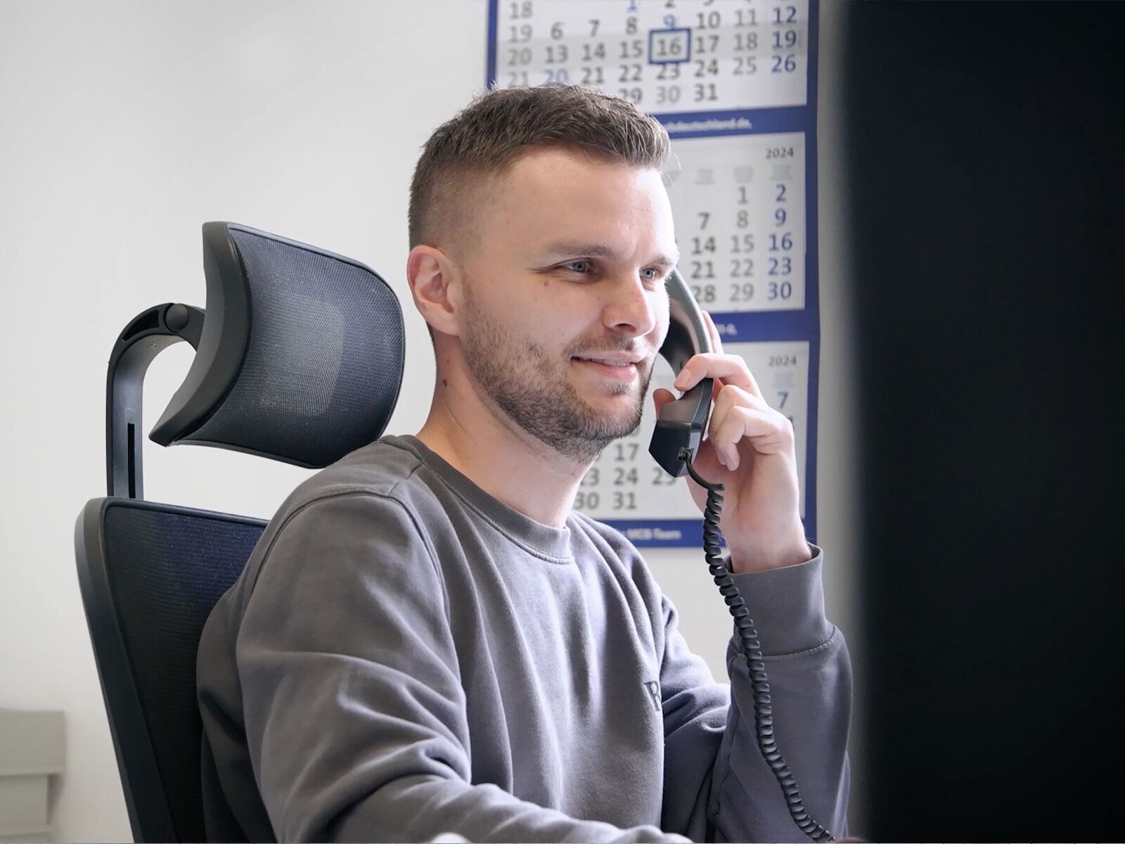 Medewerker op kantoor zit aan het bureau en telefoneert met een vaste telefoon      
