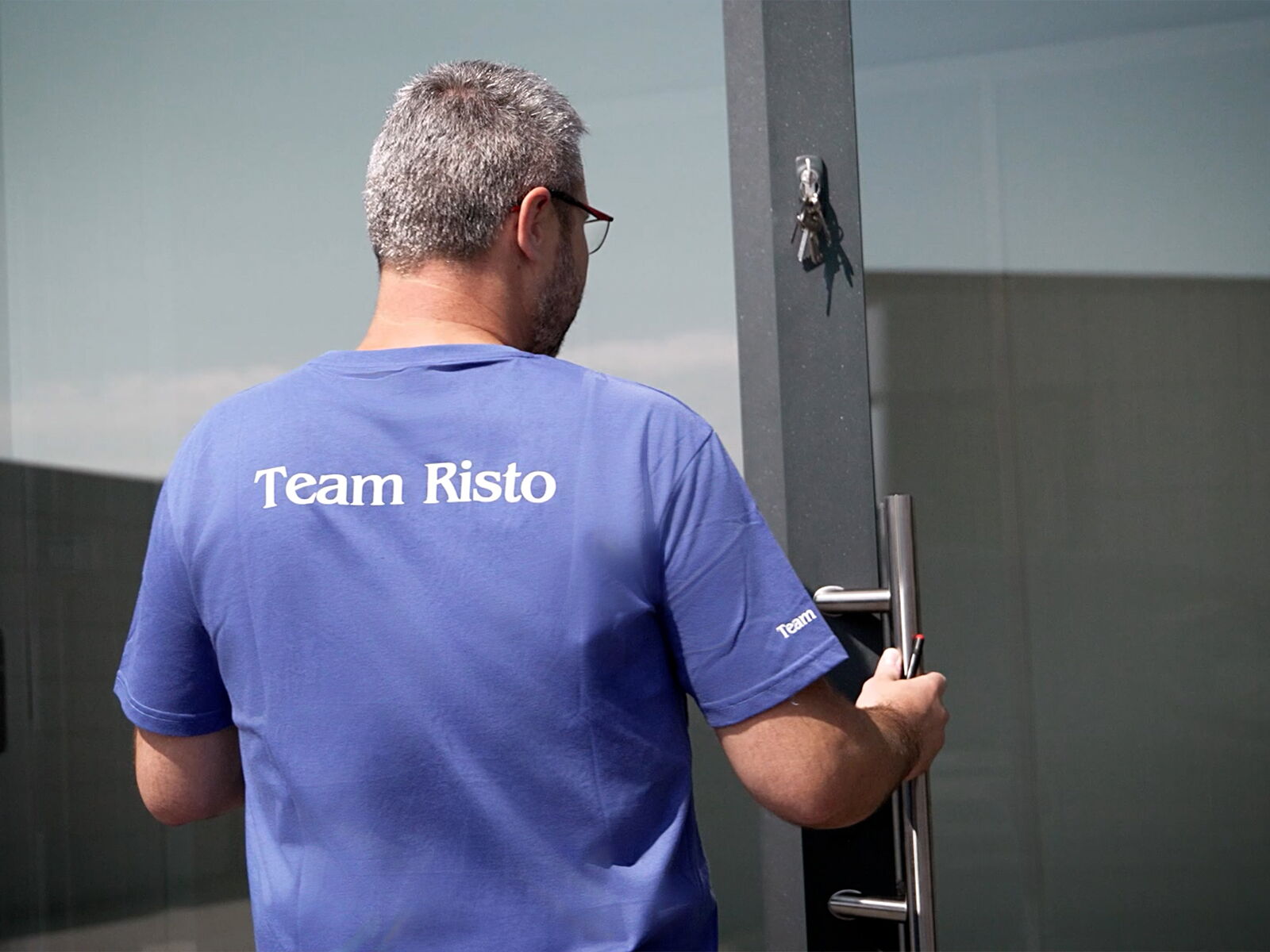 Medewerker van Risto opent een glazen deur, T-shirt met opdruk Team Risto      
