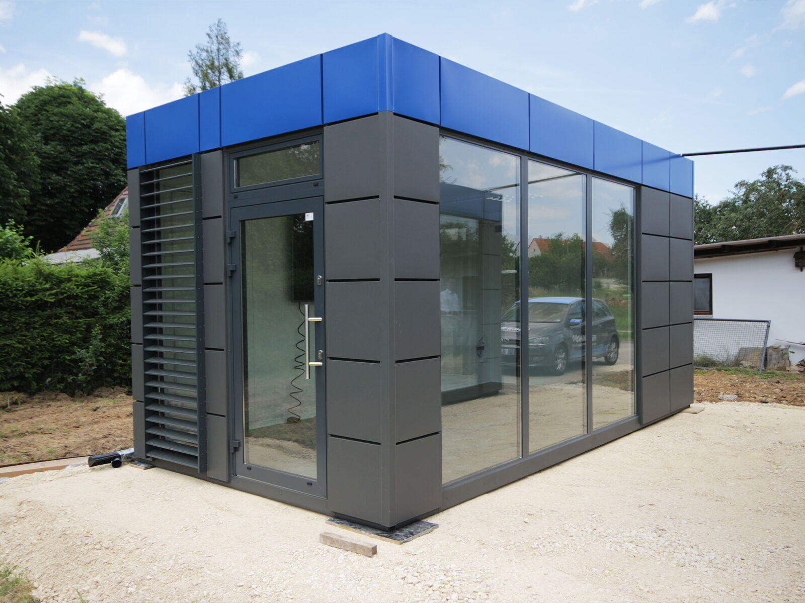Moderne kantoorcontainer met blauwe attiek en vloerdiepe glasvoorkant      